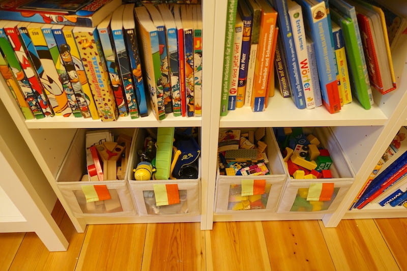 Unten im Bücherregal sind kleine Kisten für Bausteine, Spielfiguren, Murmelbahn und Playmobil. | Mehr Infos zum geteilten Kinderzimmer auf Mamaskind.de