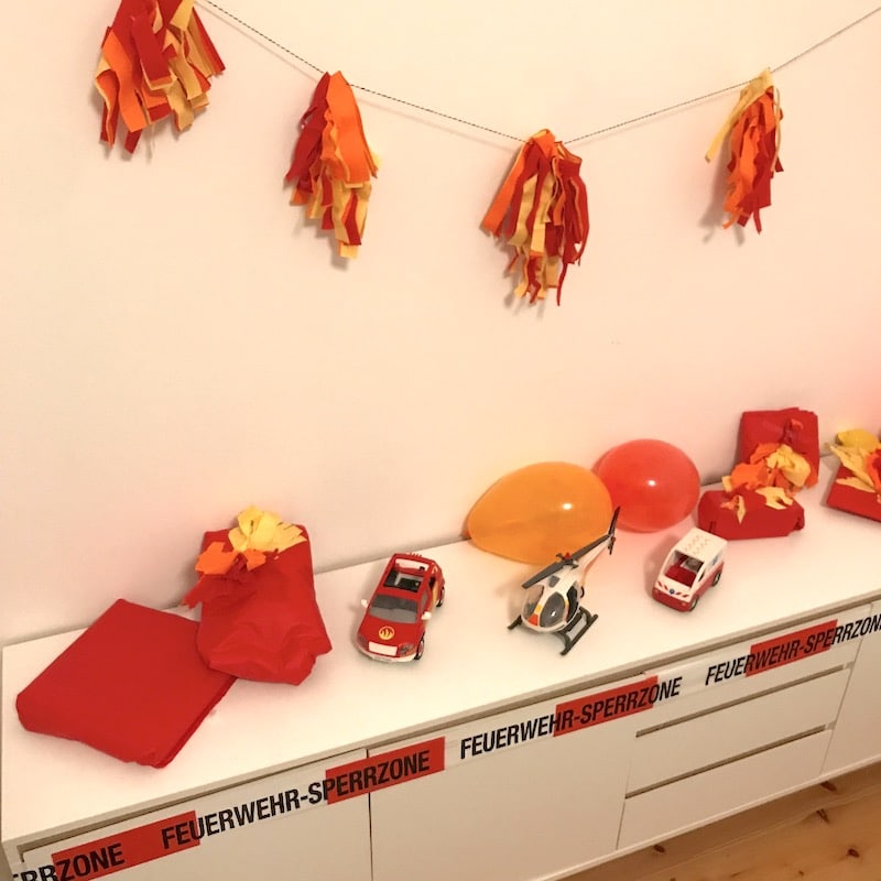 Deko zur Feuerwehr-Party: Tassel-Girlande, Luftballons, Geschenke in Seidenpapier und Absperrband. | Mehr Infos zu unserer Deko, Spielen und dem Essen zur Feuerwehrparty auf Mamaskind.de