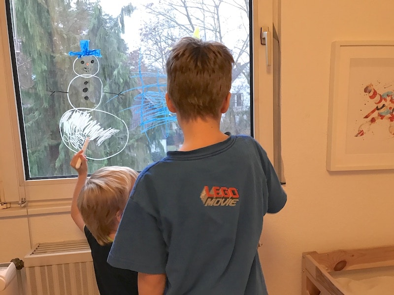 Harmonie: Die Jungs malen ein Kinderzimmerfenster mit Weihnachtsbildern an | Mehr Infos zur Fensterdeko mit Schneemann auf Mamaskind.de