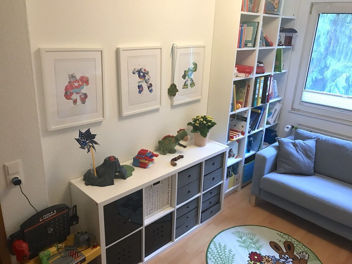 Wenig Deko im Kinderzimmer, da die Spielsachen und Bücher schon sehr bunt sind. Dezente Aquarell-Malereien von Transformers-Figuren an der Wand. - Mehr zum geteilten Kinderzimmer auf Mamaskind.de
